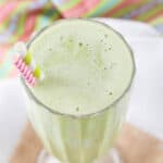 Looking down at the top of a green mint smoothie in a glass with two straws, one pink and white striped and one green and white striped.