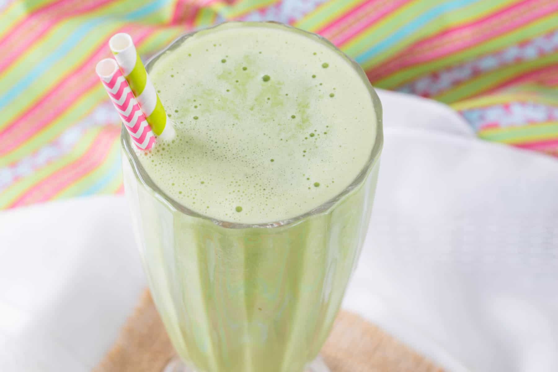 A shamrock shake smoothie in a glass with a pink and white straw and a green and white straw.