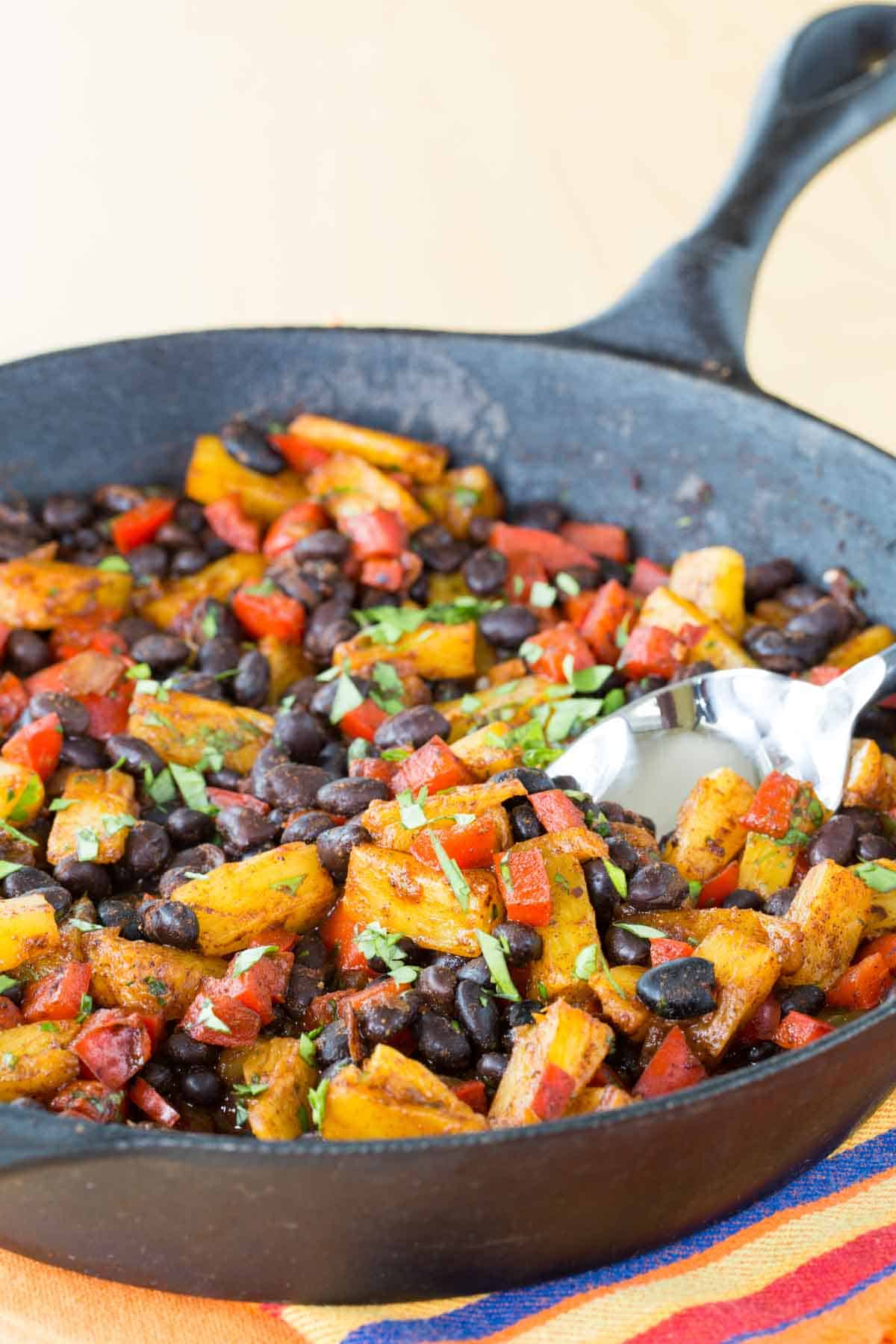 A cast iron skillet of black beans with pineapple, red pepper, and cilantro.