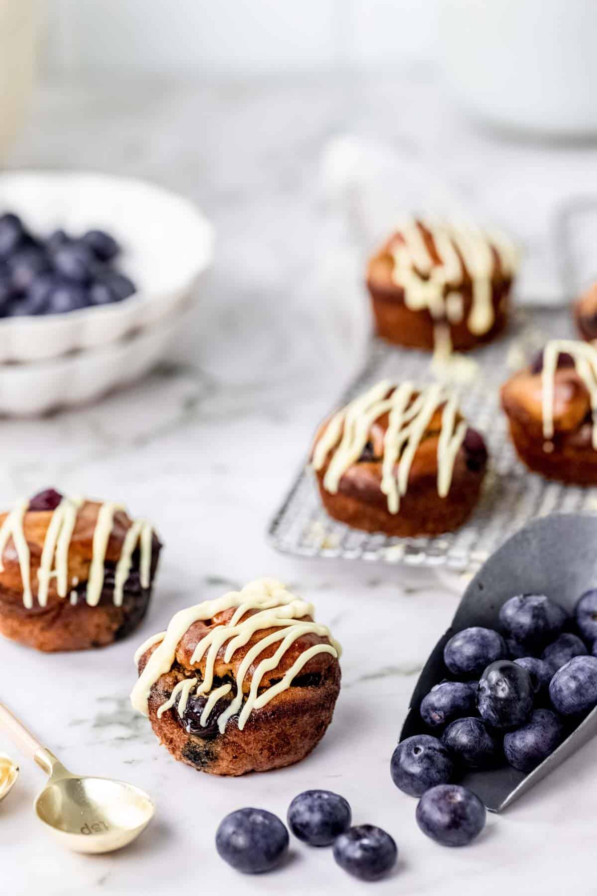 Assorted flourless blueberry mini muffins on a countertop surrounded by a bowl and a scoop of blueberries.