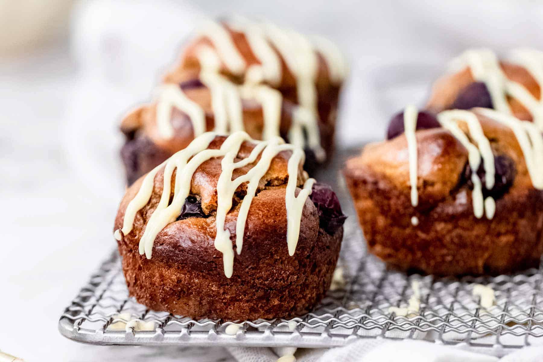 Flourless blueberry mini muffins on a wire rack, drizzled with maple cream cheese.