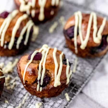 Flourless blueberry mini muffins on a wire rack, drizzled with maple cream cheese.