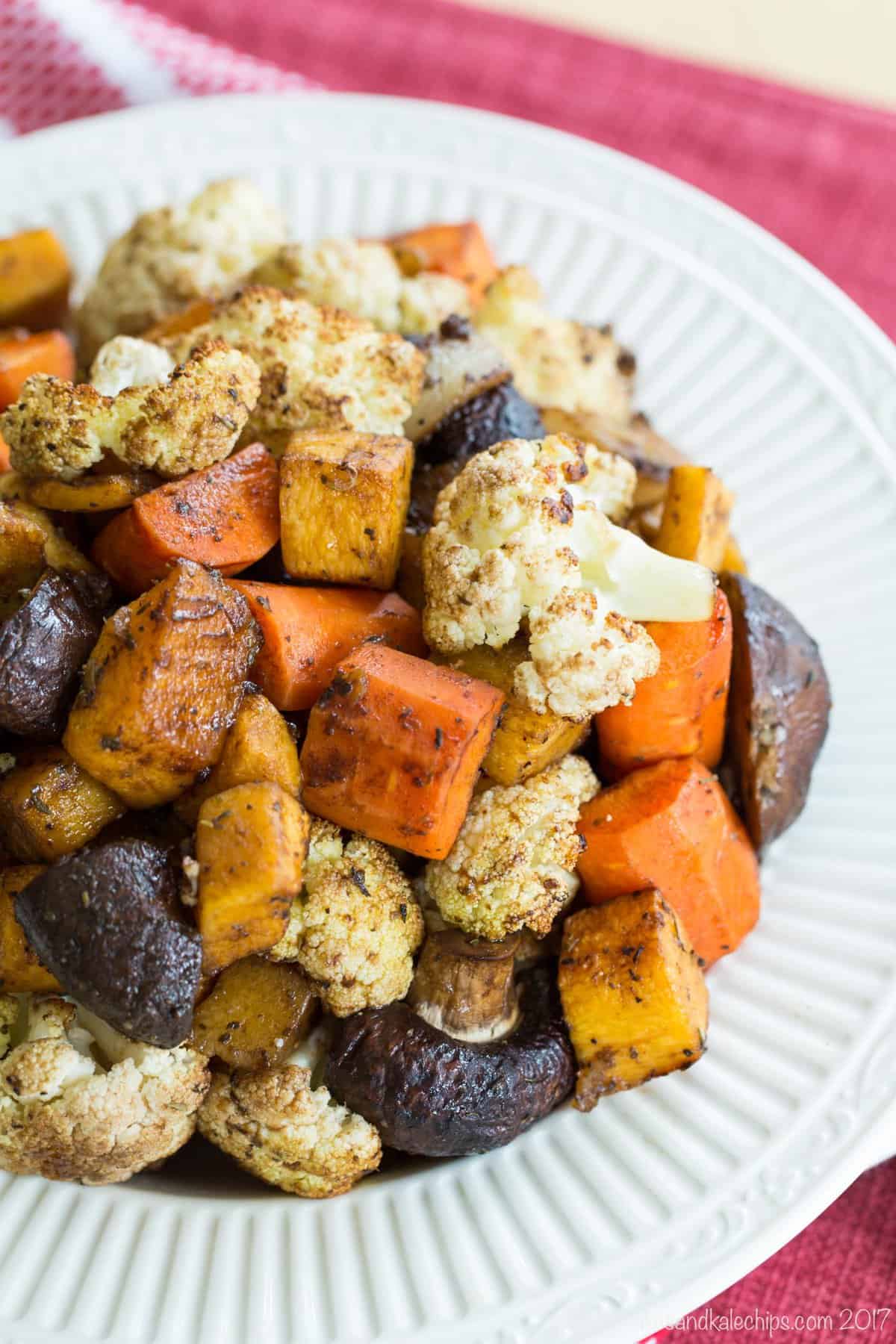 Looking down at a bowl of Balsamic Roasted Vegetables on a red placemate.