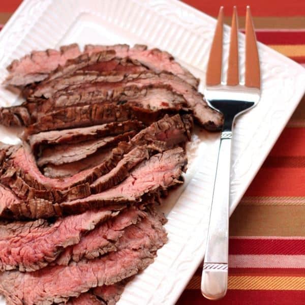 Slices of grilled flank steak on a platter with a meat fork