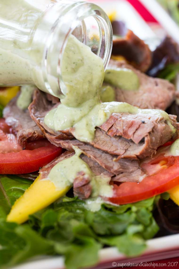 Pouring Avocado Ranch Dressing over a steak salad with mango and tomato slices