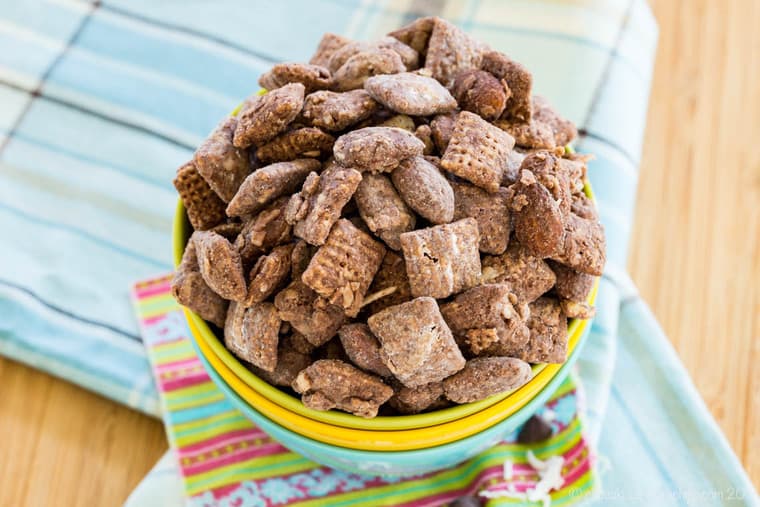 A stack of bowls with the top one full of almond butter muddy buddies with coconut and chocolate