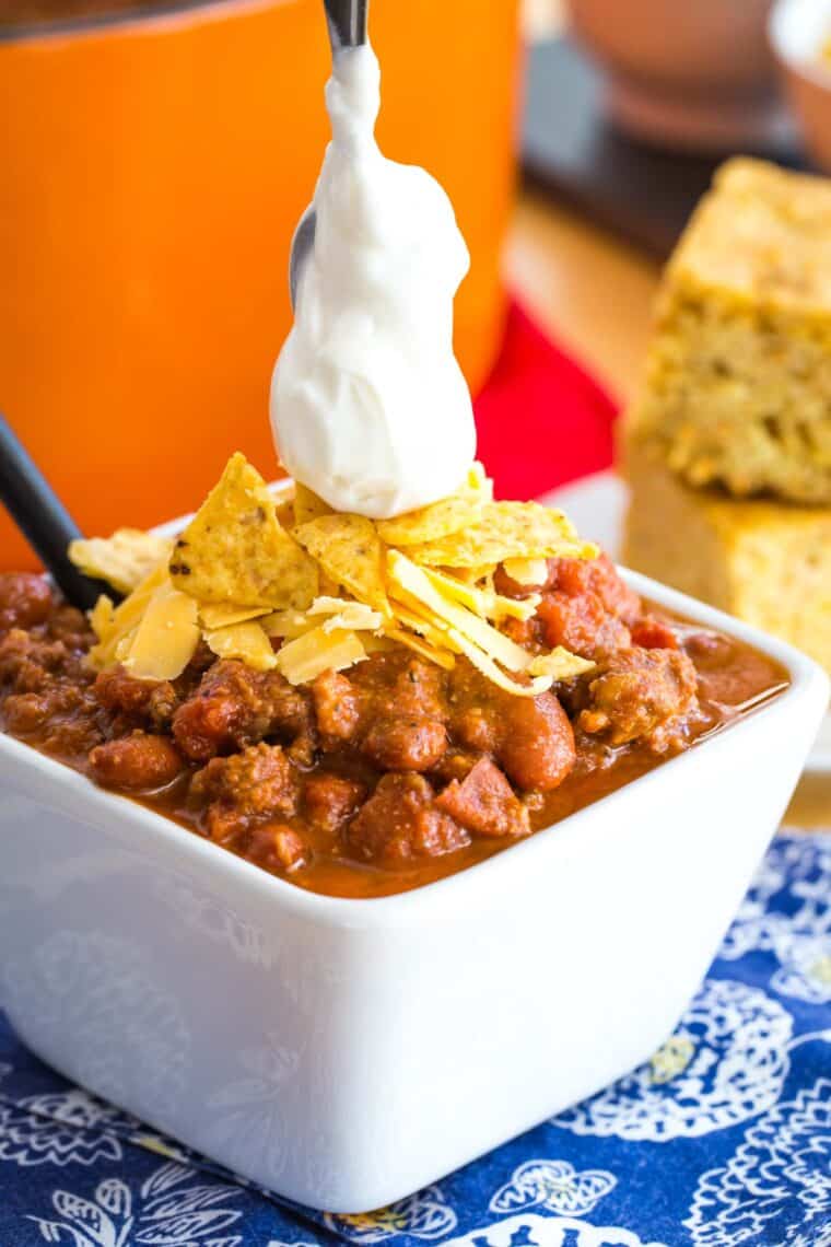 small spoon putting a dollop of sour cream on top of a bowl of chili