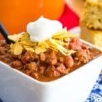 a bowl of the world's best chili on a blue cloth napkin with an orange Dutch oven behind it