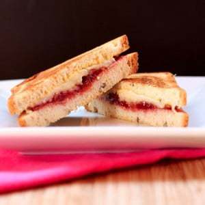 A Close-Up Shot of a Havarti Grilled Cheese Sandwich with Bacon & Strawberry Cut Diagonally Into Two Halves