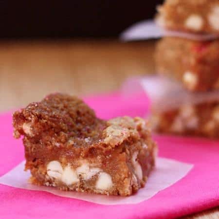 A gooey bar on a piece of parchment paper over a pink cloth with more bars stacked on the background.