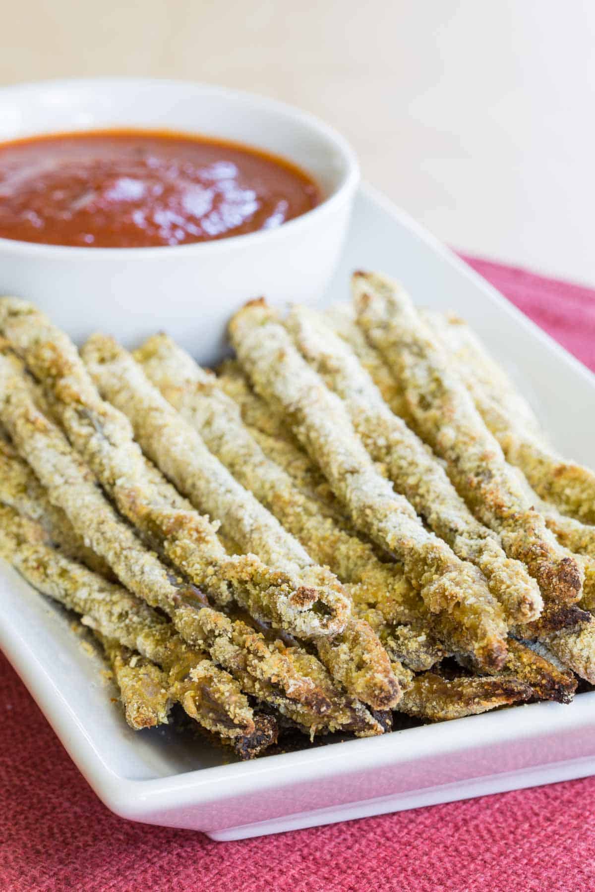 A plate of asparagus fries with a bowl of marinara sauce.