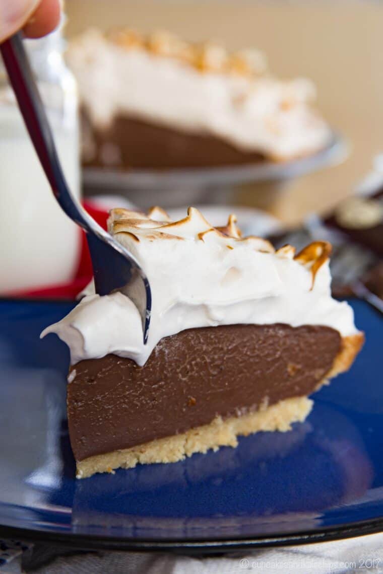 A fork digging into the corner of a slice of gluten-free s'mores pudding pie on a blue plate.