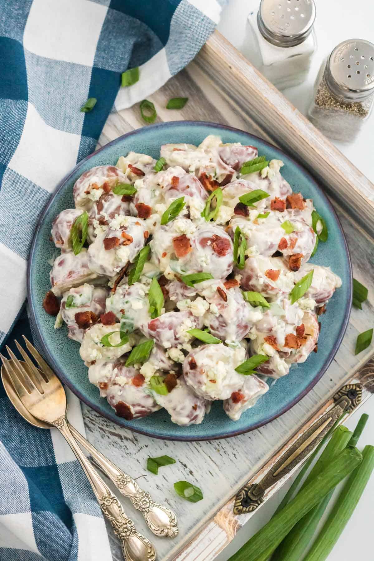 A plate full of blue cheese and bacon potato salad on a wooden tray next to a fork.