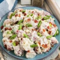 A plate full of blue cheese and bacon potato salad on a wooden tray next to a fork.