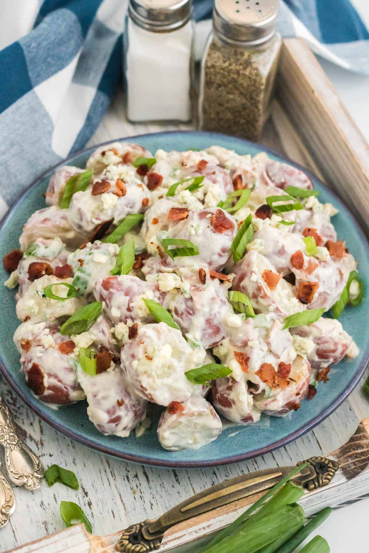 A plate full of blue cheese and bacon potato salad on a wooden tray next to a fork.
