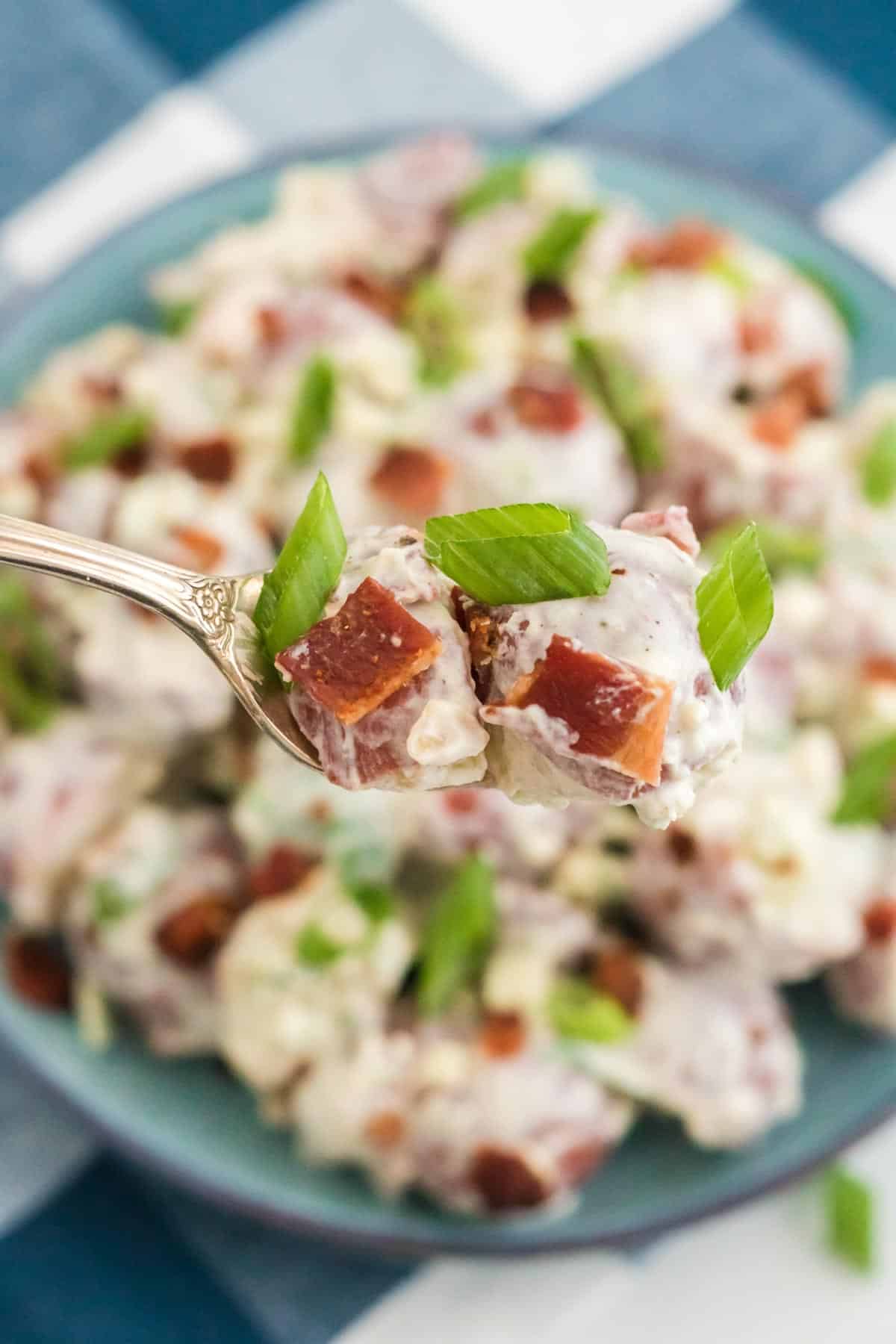 A forkful of potato salad in the foreground with potato salad in the background.