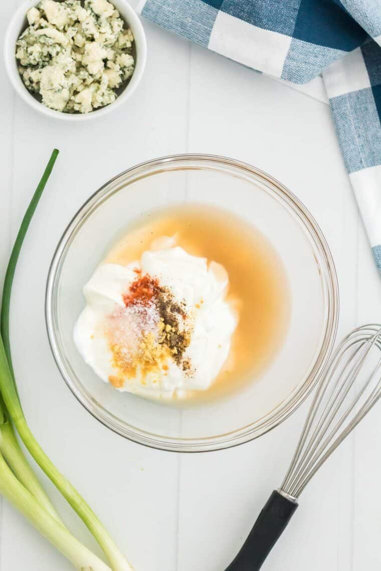 Potato salad dressing ingredients combined in a clear mixing bowl, next to a whisk.