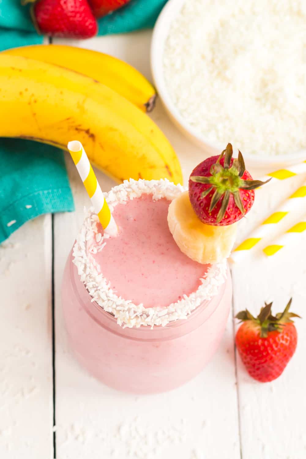 Overhead of Strawberry Banana Coconut Smoothie in a garnished glass on a white tabletop.