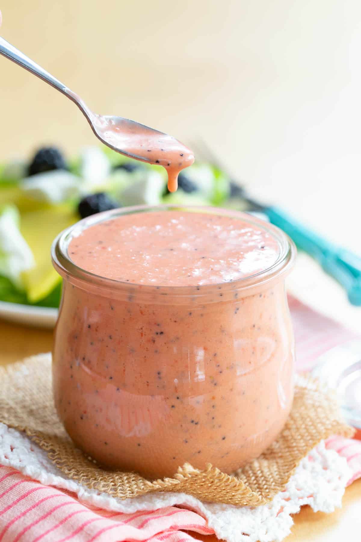 The finished salad dressing dripping off a spoon into a jar.