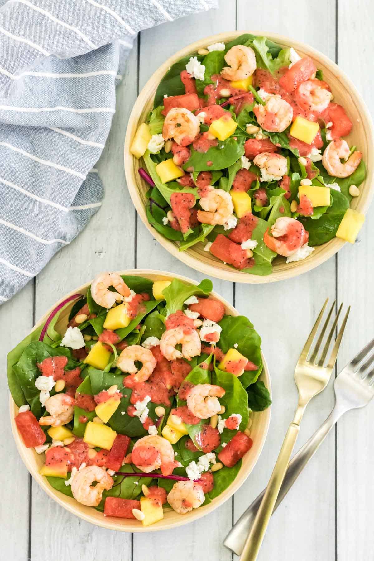 two wooden bowls of grilled shrimp salad with fruit, pine nuts, goat cheese, and strawberry poppyseed dressing with two forks