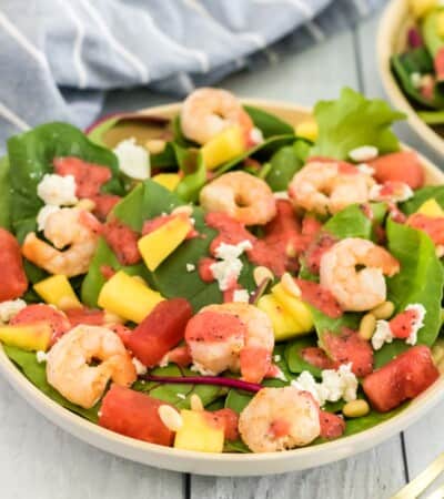 bowl of mixed greens topped with grilled shrimp, watermelon, mango, pineapple, crumbled goat cheese, pine nuts, and strawberry vinaigrette