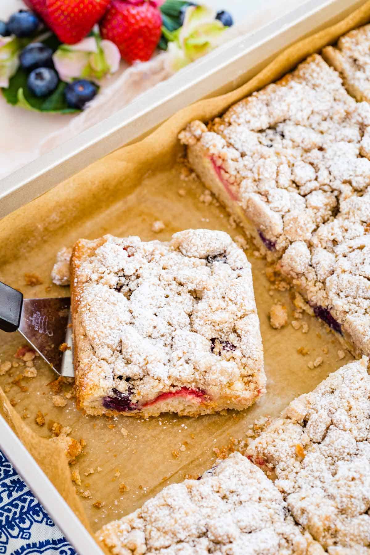 A slice of crumb cake is served from the rest of the cake in a baking pan.