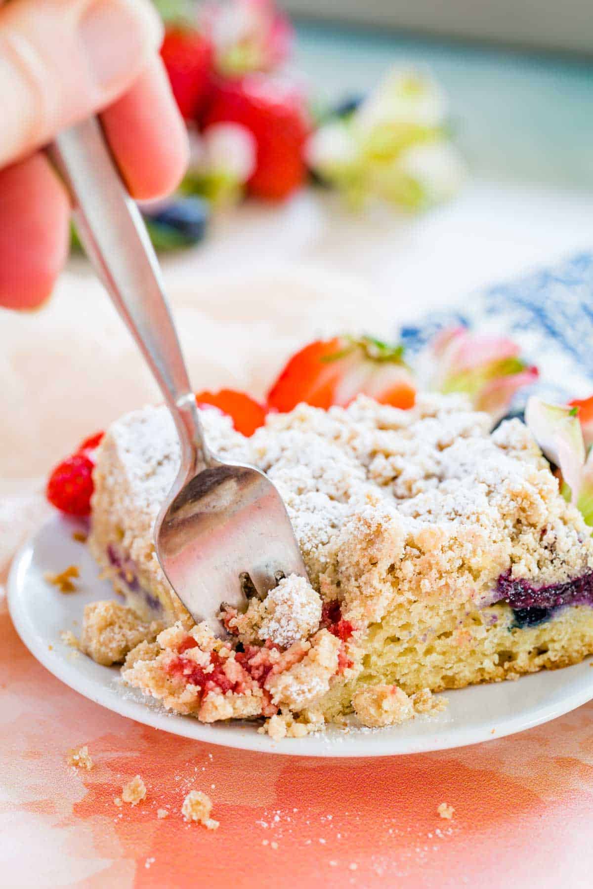 A fork poked into the corner of a slice of crumb cake on a plate.