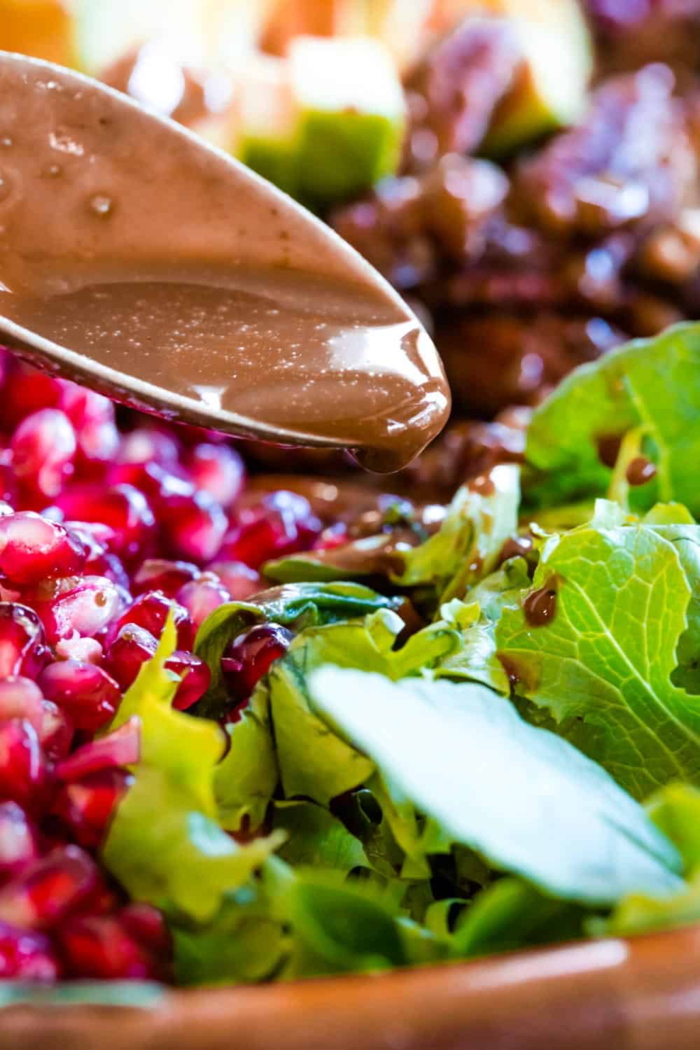 Drizzling the cranberry vinaigrette off a spoon onto a salad.
