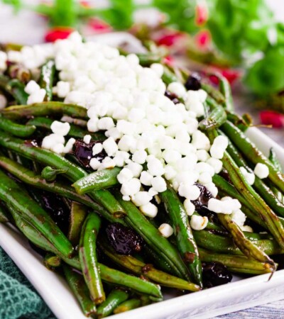 Balsamic Green Beans with Cranberries on a white rectangular serving dish topped with goat cheese