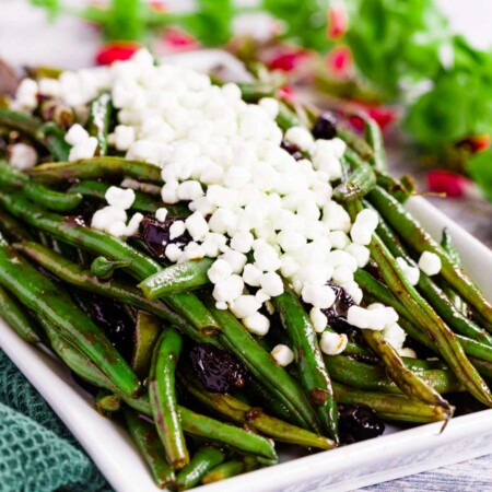 Balsamic Green Beans with Cranberries on a white rectangular serving dish topped with goat cheese