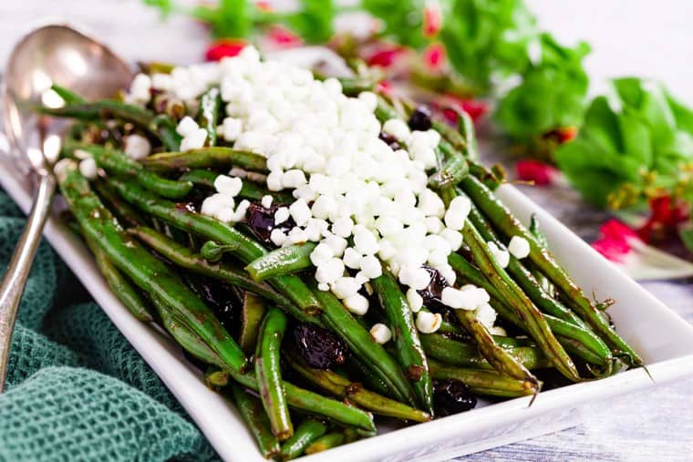 Balsamic Green Beans with Cranberries on a white rectangular serving dish topped with goat cheese