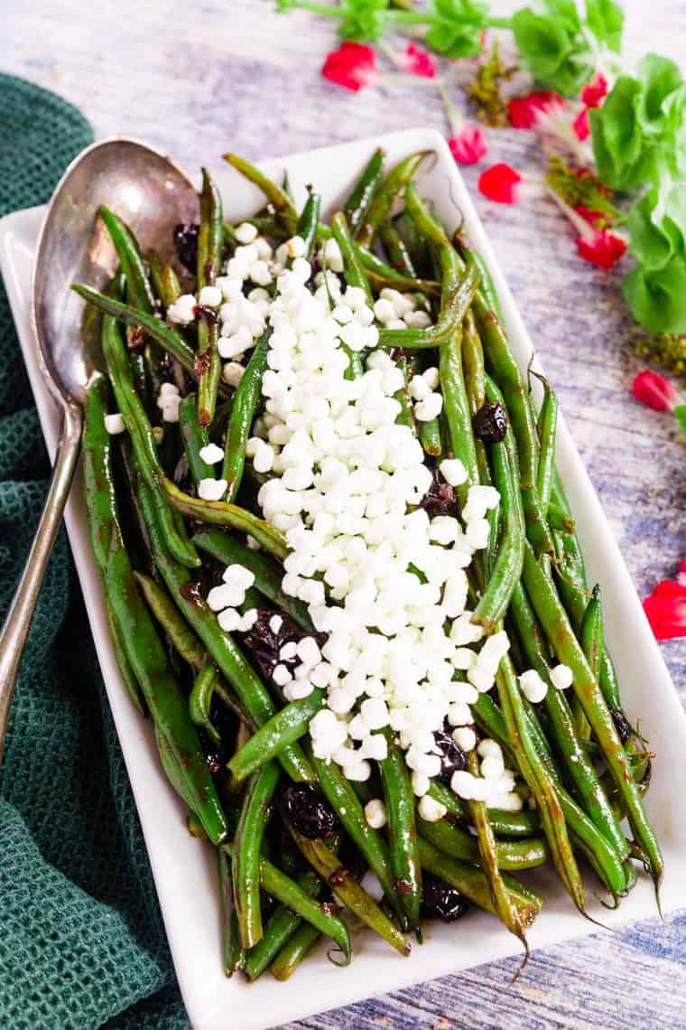 A white rectangular platter full of balsamic glazed green beans with a silver serving spoon