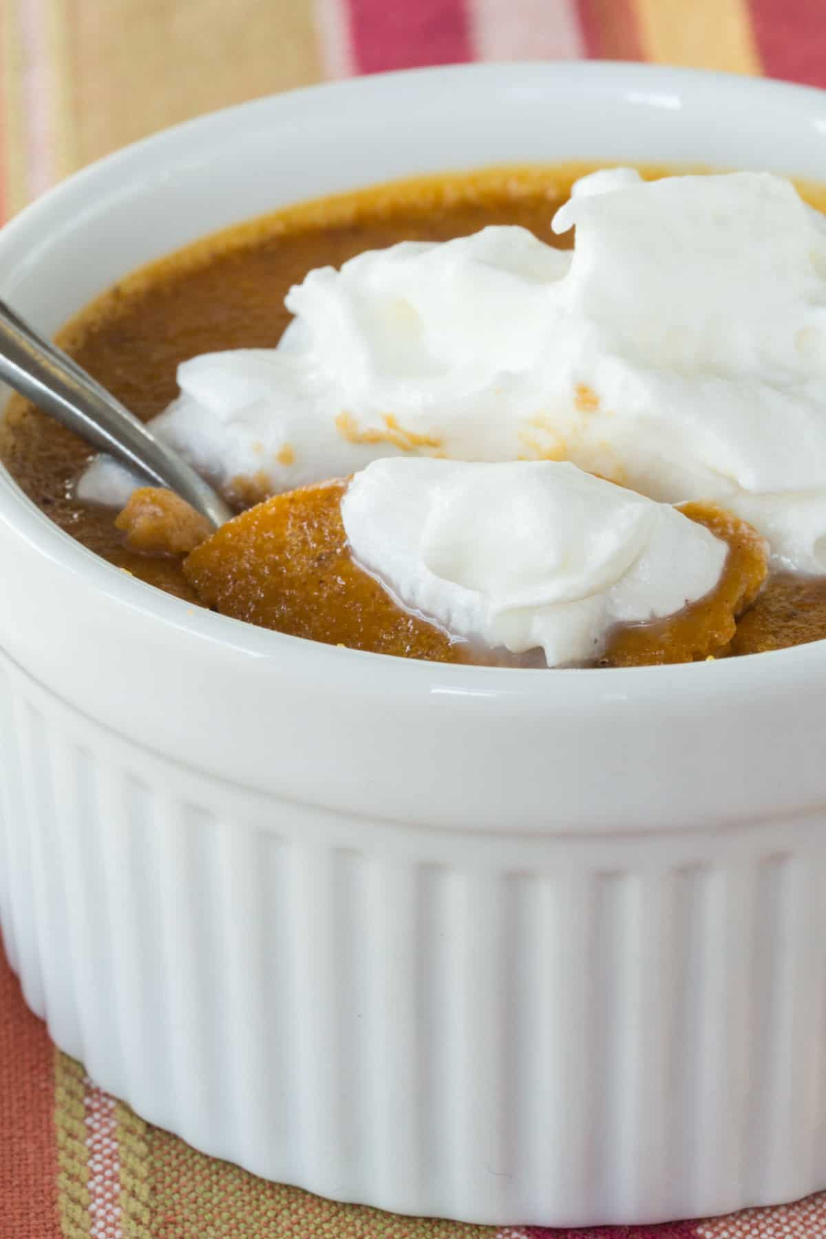 spoon going into the top of a a mini crustless pumpkin pie in a ramekin topped with whipped cream