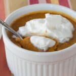 A spoon resting in a ramekin of pumpkin custard topped with whipped cream.