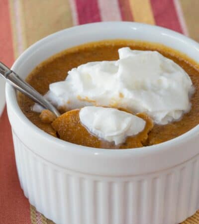 A spoon resting in a ramekin of pumpkin custard topped with whipped cream.