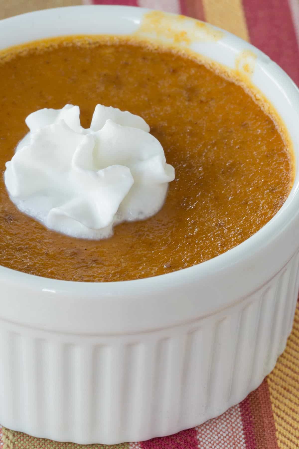closeup of the top surface if the pumpkin custard in a ramekin with a bit of whipped cream on top