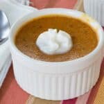 Pumpkin custard in a ramekin on a striped placemat with a cloth napkin and a small spoon next to it