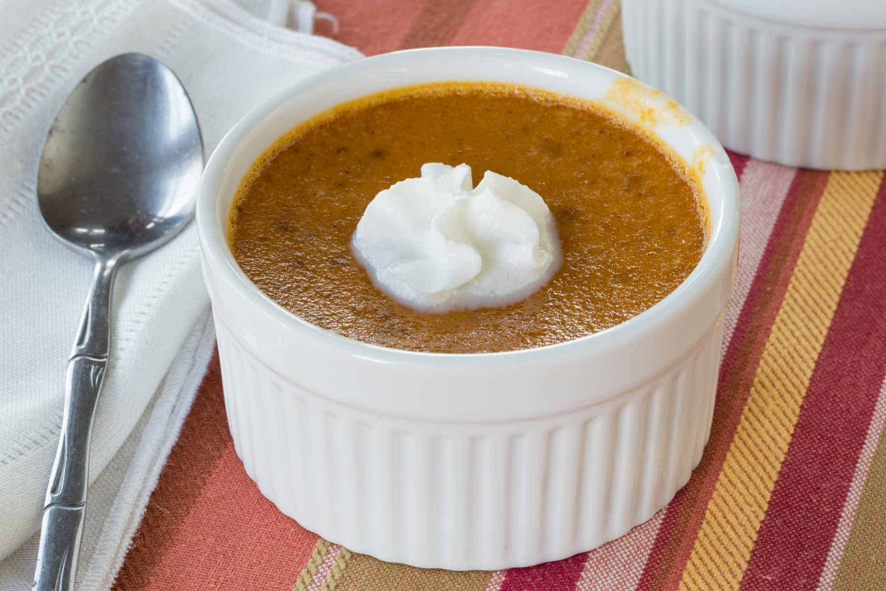 Pumpkin custard in a ramekin on a striped placemat with a cloth napkin and a small spoon next to it