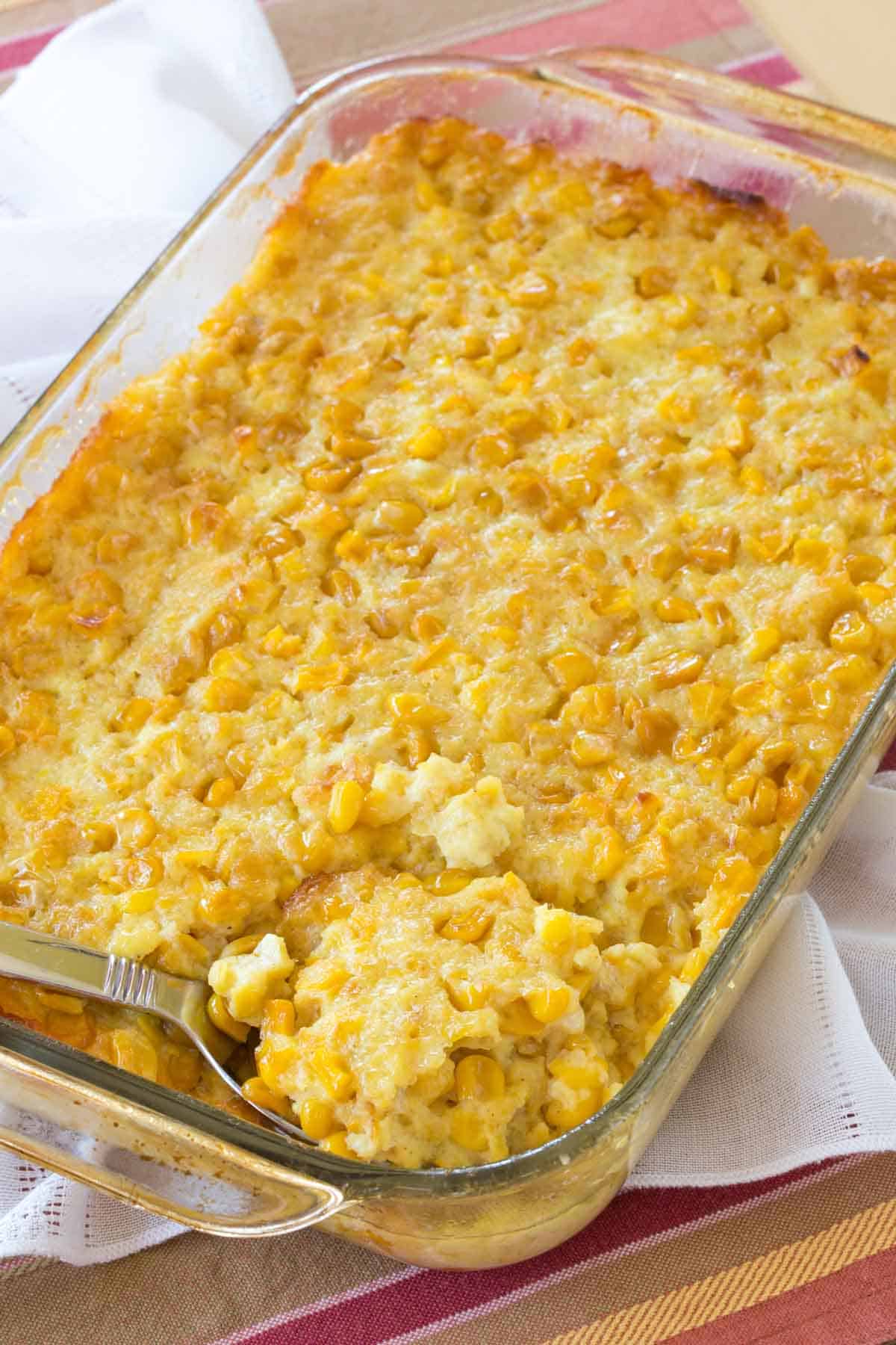 Looking down at the baking dish of corn pudding on top of a lacy cloth napkin and a striped placemat.