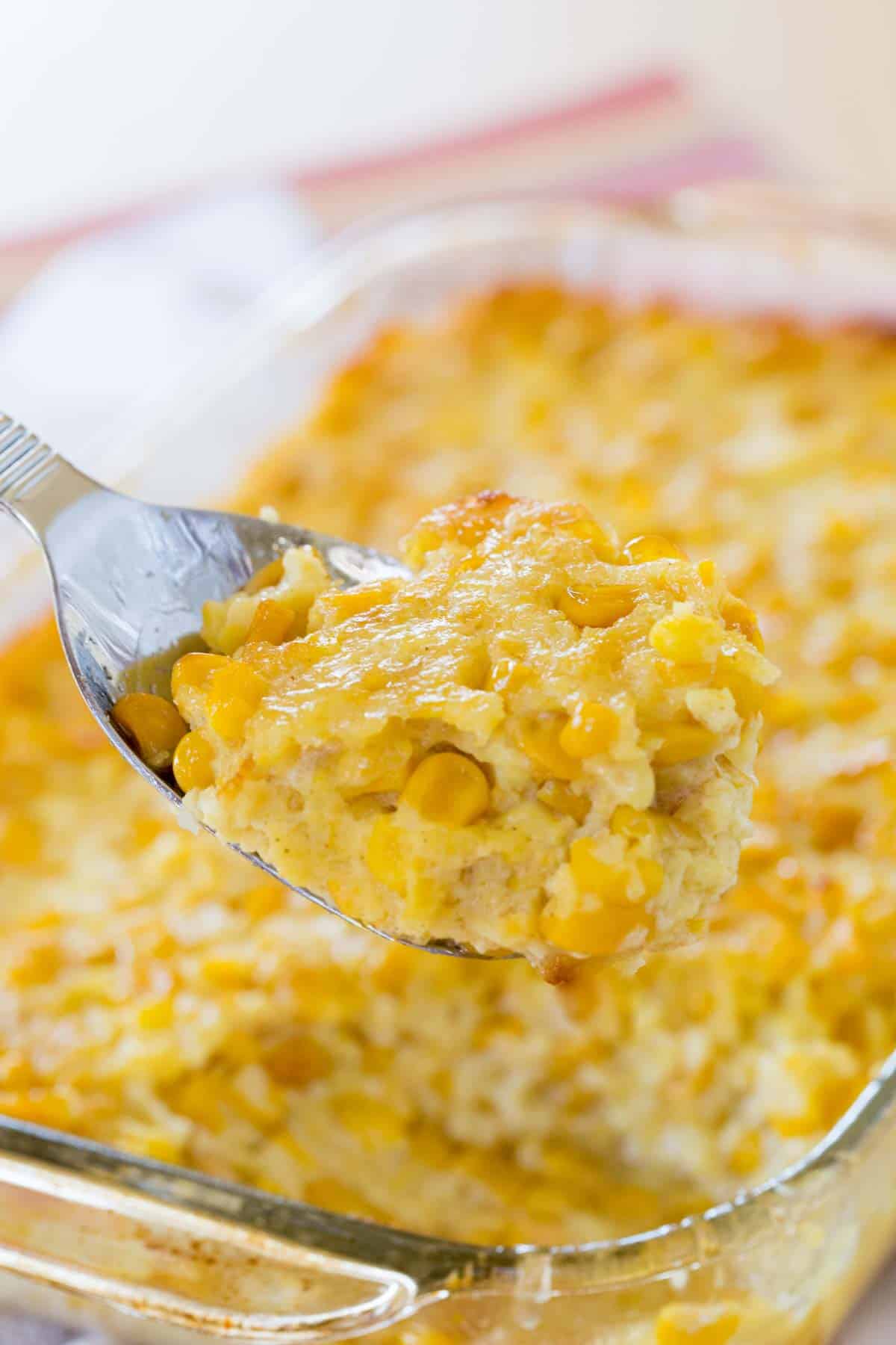 A scoop of corn pudding on a spoon over the casserole dish.