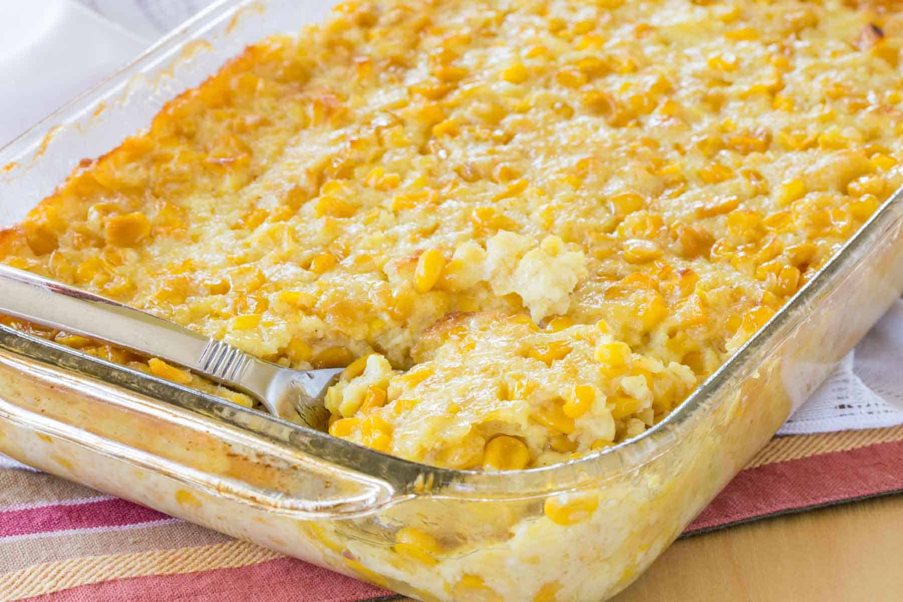 Corn pudding casserole in a glass pan with a spoon laying in it.