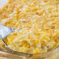 A spoon scooping up some corn pudding out of a glass baking dish.