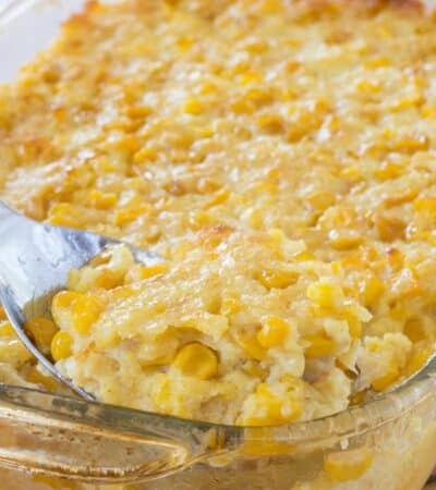 A spoon scooping up some corn pudding out of a glass baking dish.