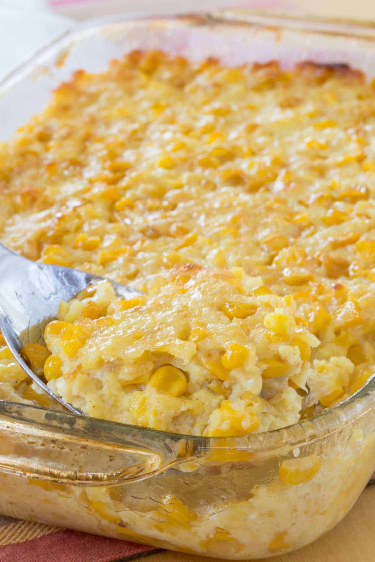 A spoon scooping up some corn pudding out of a glass baking dish.