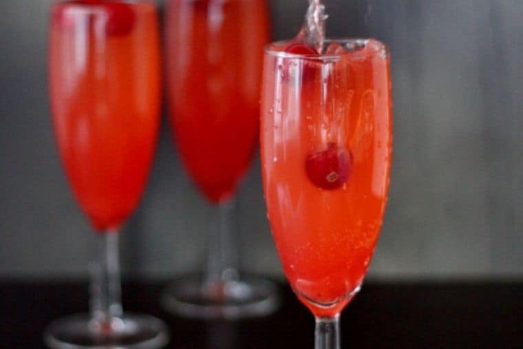 A red Christmas Mocktail in a flute with a fresh cranberry in it, with two more in the backgrund.