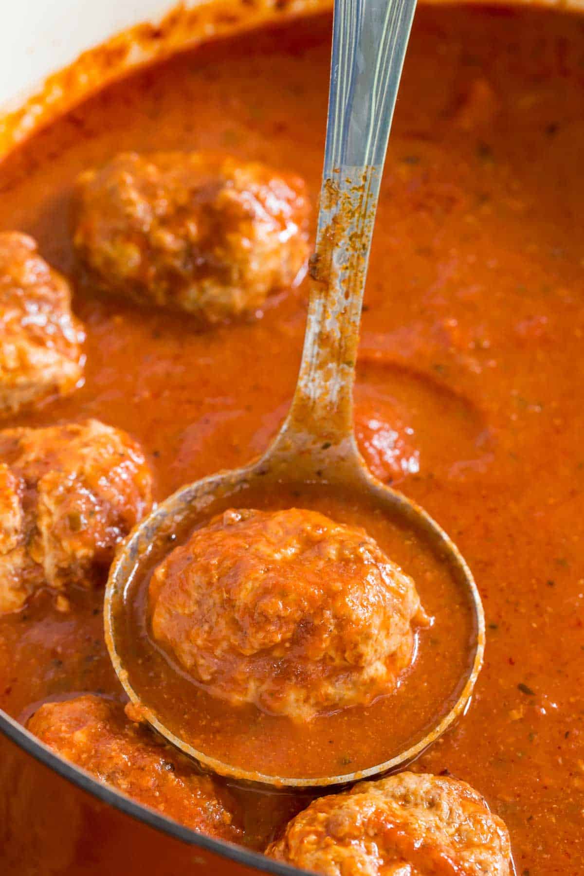 A ladle scooping an Italian meatball from a pot filled with meatballs and marinara sauce.