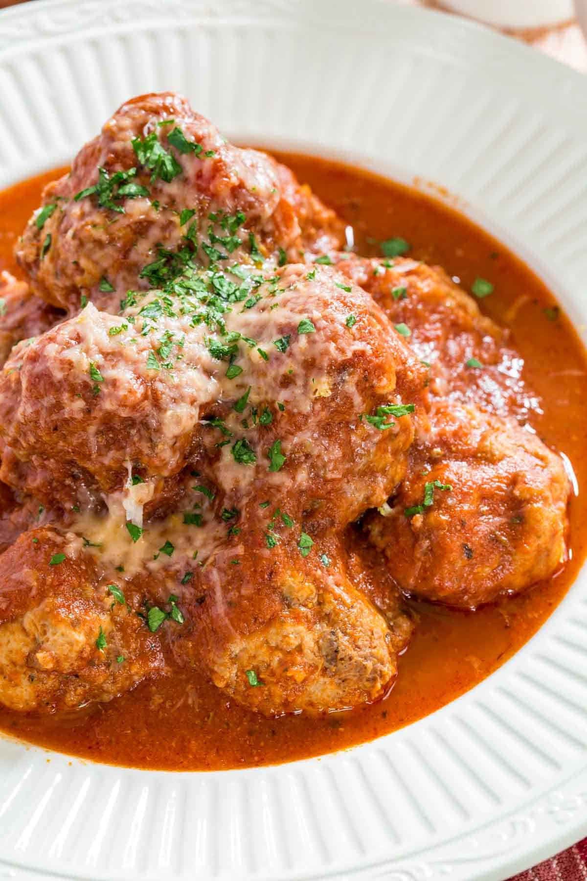 Italian meatballs in marinara sauce in a bowl, garnished with parmesan and parsley.