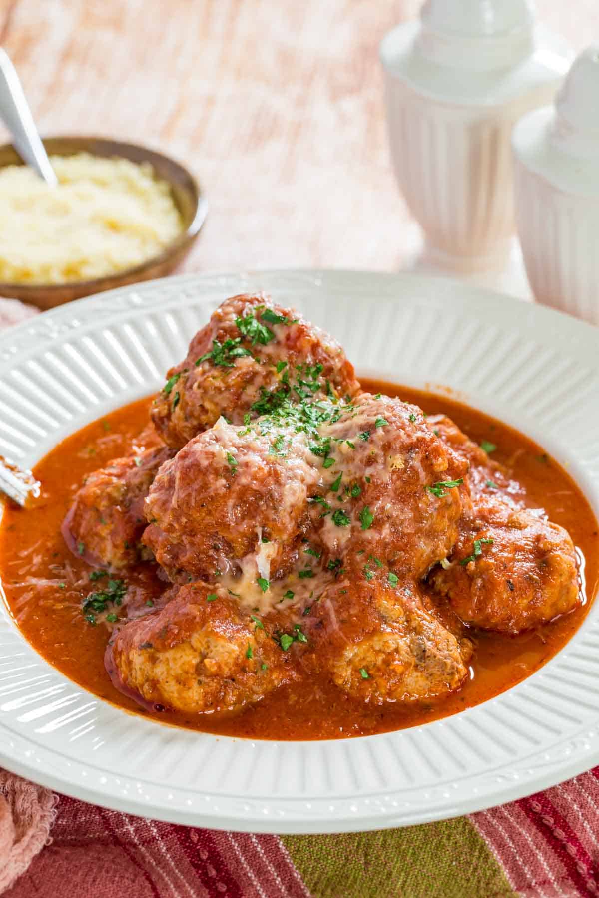 Italian meatballs in marinara sauce in a bowl, garnished with parmesan and parsley.