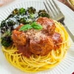 A plateful of spaghetti and Italian meatballs with a side of roasted broccoli, topped with parmesan next to a fork.