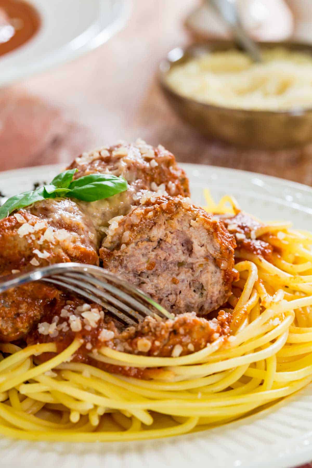 A fork cuts into an Italian meatball on top of a plate of spaghetti.